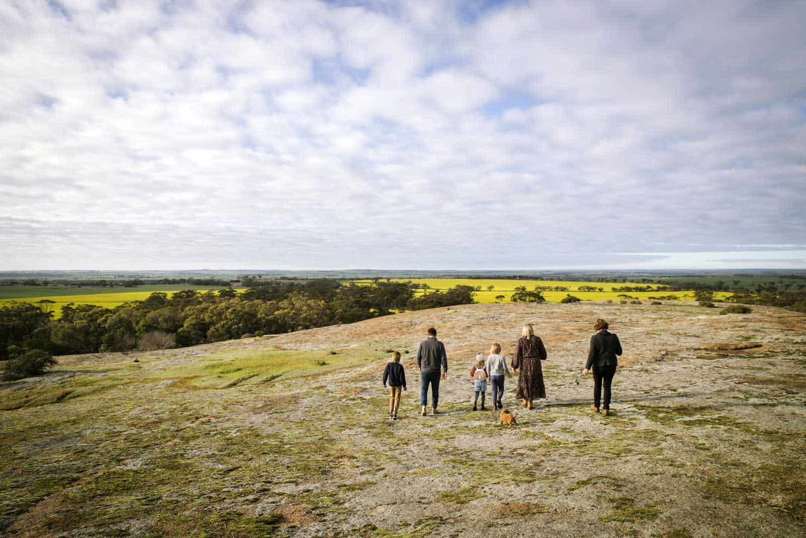 Group of people walking on top of a rock with canola fields in the distance in Corrigin on the Pathways to Wave Rock